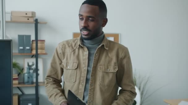 Homme d'affaires afro-américain confiant marchant dans le bureau parler à ses collègues puis en utilisant un ordinateur portable — Video