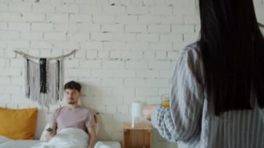 Bakıcı kadın, kocası televizyon izlerken adama yemek tepsisi getiriyor.