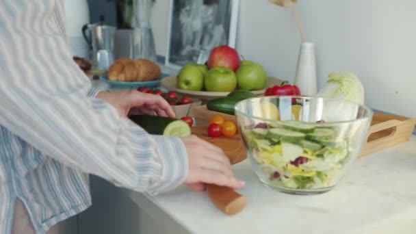 Großaufnahme weiblicher Hände beim Gurkenschneiden in der Küche, während Hausfrau Salat kocht — Stockvideo