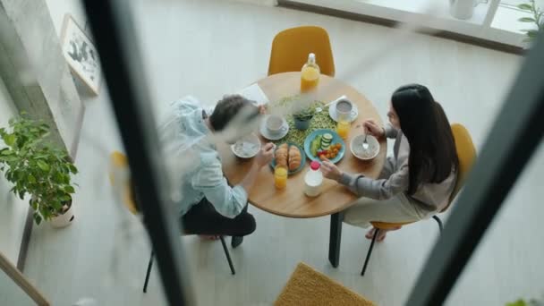 Κάτοψη των νεαρών συζύγων να τρώνε φαγητό για πρωινό και να μιλάνε στην κουζίνα στο διαμέρισμα — Αρχείο Βίντεο