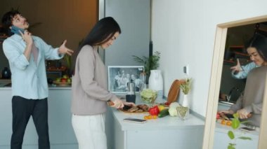 Genç kadın yemek pişirirken, sevgili koca cep telefonuyla sohbet ederken ve mutfakta karısını öperken.