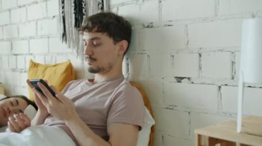 Karışık ırk adamı akıllı telefon kullanıyor. Kadın evde yatarken ekrana dokunuyor.