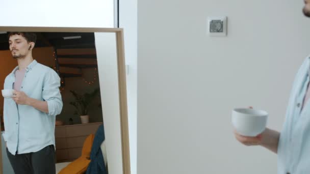 Όμορφος τύπος πίνοντας καφέ και βλέποντας την πόλη από πανοραμικό παράθυρο στο διαμέρισμα — Αρχείο Βίντεο