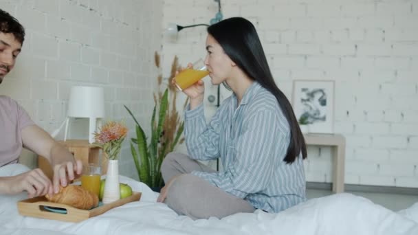 Chica y chico desayunando y hablando sonriendo en la cama en el apartamento — Vídeo de stock