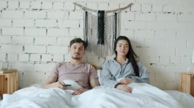 Sıkılmış çiftin portresi tavan arası yatak odasında televizyon kanallarını değiştiriyor.