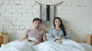 Mutlu çift portresi yatakta televizyon seyrediyor, gülüyor ve evde eğleniyor.