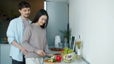 Genç bir kadın sebze kesiyor salata pişiriyor sonra mutfakta kocasını öpüyor ve sarılıyor.