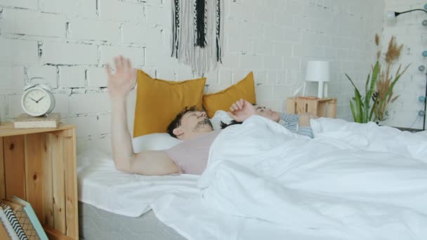 Hombre despertando chequeando reloj empujando esposa y corriendo al trabajo por la mañana — Vídeos de Stock