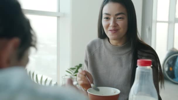Felice donna asiatica mangiare cereali per la prima colazione e parlare con il marito sorridente in cucina a casa — Video Stock