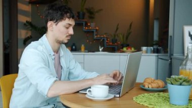 Dizüstü bilgisayarla çalışan ve mutfak masasında kahve içen ciddi bir serbest çalışan.