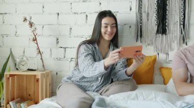 Zeki telefon kullanan Asyalı bir kadın kocasına ekranı gösterirken evde dizüstü bilgisayar kullanıyor.