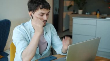 Dizüstü bilgisayarla çalışan ve evdeki kablosuz kulaklıklarla müziğin keyfini çıkaran serbest çalışan genç bir adamın portresi.