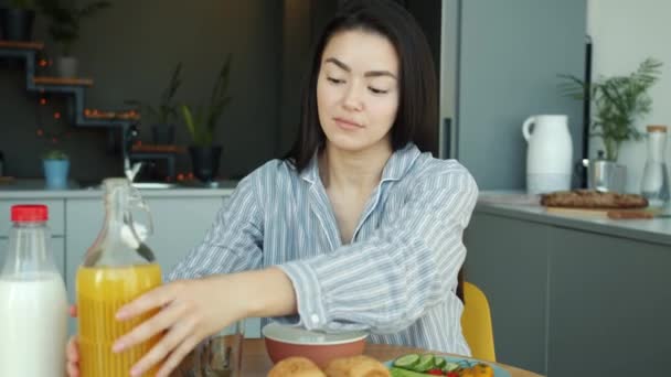 Ritratto di donna asiatica spensierata che versa succo di frutta nel bicchiere durante la colazione a casa — Video Stock