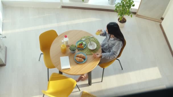 Vista dall'alto della signora spensierata che fa colazione a casa e utilizza lo smartphone godendo dei social media — Video Stock