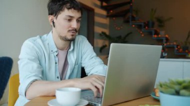 Evde dizüstü bilgisayar ve kulaklık kullanan genç bir adamın videoda konuşma portresi.