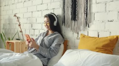 Akıllı telefon kullanan ve evde kulaklıkla müzik dinleyen göz bantlı sevimli Asyalı kadının portresi.