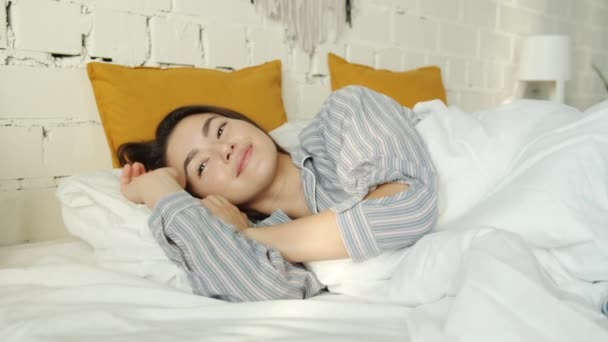 Cámara lenta de la mujer asiática durmiendo y luego despertando sonriendo y estirándose en la cama en casa — Vídeo de stock