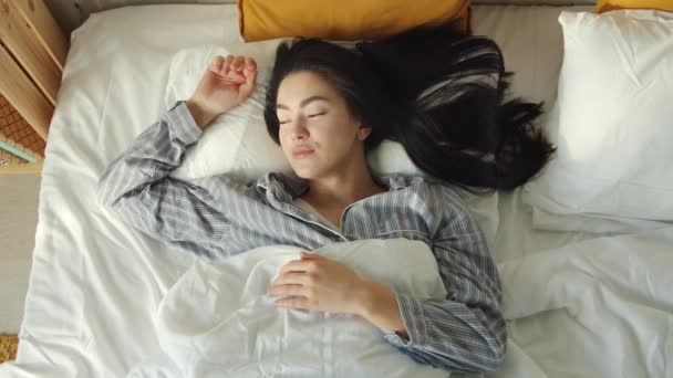 Vista superior de la joven mujer asiática linda durmiendo y luego despertando y estirando los brazos en la cama cómoda — Vídeo de stock