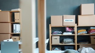 Raflarda kullanılmış giysiler, karton kutular ve içinde insan olmayan yardım fonu ofisleri olan bir depo. Gönüllülük ve iş konsepti.