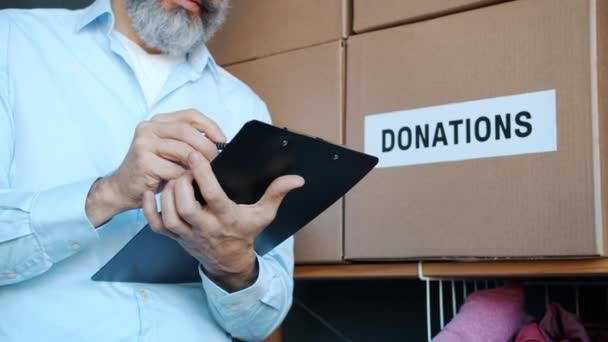 在剪贴板上写慈善基金经理的特写 带着捐款箱在储藏室里进行盘点 志愿人员工作和人道主义援助概念 — 图库视频影像