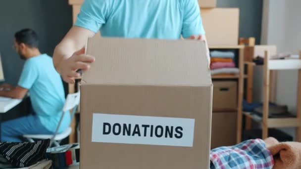 在慈善公司工作的身着制服包装捐款箱的志愿者的特写镜头 而同事则以电脑为背景 行动主义和社会支助概念 — 图库视频影像