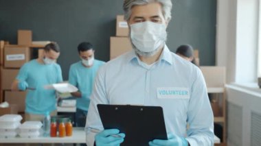 Bağış fonu yöneticisinin yavaş çekimde portresi, arka planda yemek paketleyen gönüllülerin elinde panoyla içeride duruyor. Meslek ve insanlar kavramı.