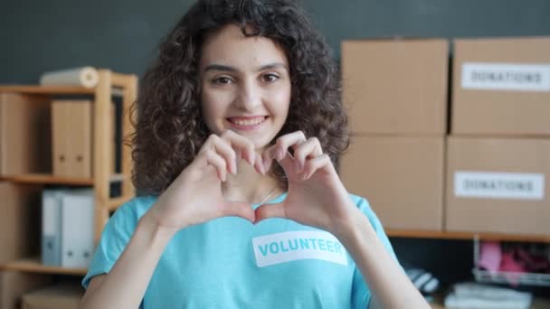 在慈善公司的办公室里 以捐赠盒为背景 制作了快乐的年轻女性志愿者的慢动作肖像画 并做出了感人的手势和微笑 — 图库视频影像