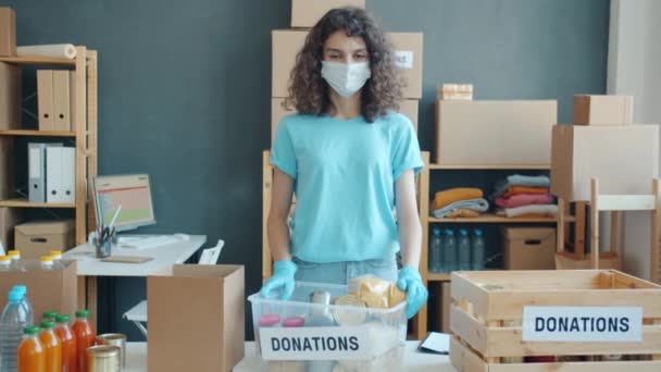 身穿面部面具的女志愿者慢镜头 站在慈善基金办公室食物捐赠处 看着镜头 人与社会支助概念 — 图库视频影像