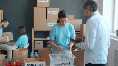 Konteynırda yiyecek paketleyen gönüllü ve ofisteki hayır kurumu yöneticisiyle konuşan biri. İnsani yardım ve gönüllü çalışma kavramı.