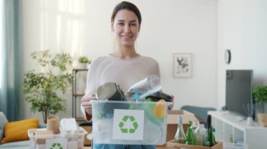 Evde durup kameraya bakmak için elinde plastik kapla geri dönüşüm kutusuyla gülümseyen genç bayan. İnsanlar ve ekoloji kavramı.