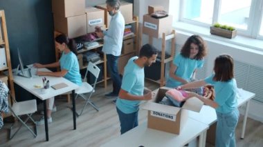 Yüksek açılı bir bakış açısıyla, aktivist öğrencilerin yardım kuruluşunda çalışmak için kullanılmış giysiler paketlediklerini görüyoruz. Fakirlere yardım etmek ve gönüllü olmak.
