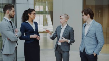 İşkadını meslektaşları duran kapalı ofis lobisinde konuşuyor. Grup gelecekteki anlaşma tartışırken iş adamları