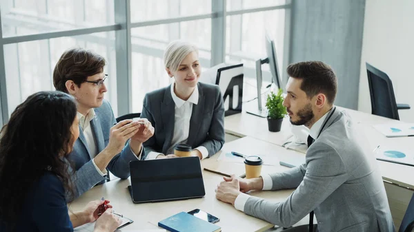 Businessman discussing future business project with male and female colleagues sitting at the table in modern office indoors