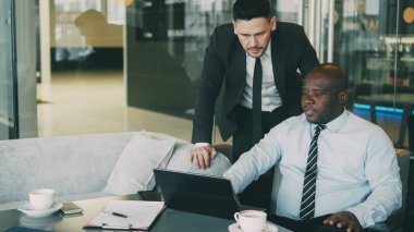 Kendine güvenen modern kafe yakın duran Afro-Amerikan ceo verir yönergeleri onun sakallı Kafkas çalışan iş için uygun. Afrika kökenli Amerikalı işadamı onun dizüstü bilgisayar işaret oturur
