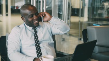 Onun smartphone üzerinde konuşmak ve onun laptop modern café'de seyir sırasında öğle yemeği zaman net tarama resmi kıyafetler Afrikalı-Amerikalı işadamı portresi. O hırslı ve başarılı görünüyor.