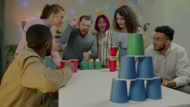 ホームパーティーで高校生を笑ってボールゲームをプレイする学生の多様なグループ 余暇には気楽なアクティビティを楽しむ男性と女性 — ストック動画