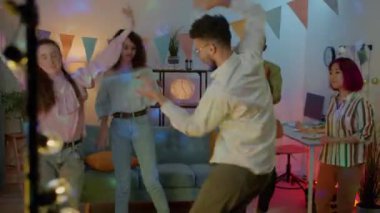 Modern evdeki gece partisinde dans eden ve müzik dinleyen mutlu öğrenci erkekler ve kadınlar. Gençlik yaşam tarzı ve eğlence konsepti.