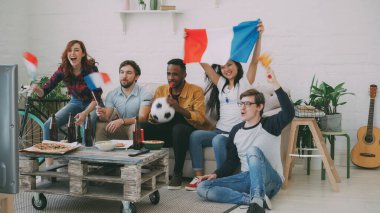 Çok etnik gruptan oluşan bir grup arkadaşıyla birlikte evde kapalı Futbol Şampiyonası TV izlerken ve favori takım tezahürat Fransız bayrakları ile sporseverler