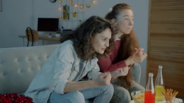 Aşırı neşeli spor hayranları TV 'de yarışmayı izleyen genç bayanlar sarılarak akşamları evde rahatça beşlik çakıyorlar. Gençlik ve eğlence etkinliği konsepti.