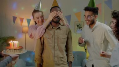 Arkadaşları ev partisinde gülerken ve el çırparken sürpriz bir Afrikalı Amerikalı adam doğum günü pastasına mum üflüyor. Kutlama ve arkadaşlık kavramı.