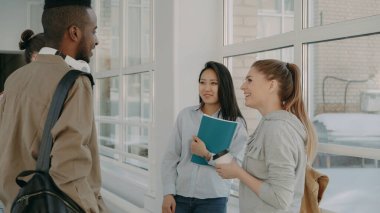 Çok etnik gruptan oluşan grup dört öğrencinin üniversitede birbirinizle olumlu şekilde, çocuklar ve kız konuşmak geniş lighty camsı salonda ayakta karınca gülen Dinkleyen kahve gülümseyen