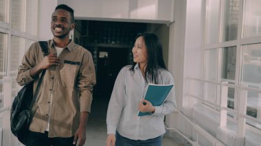 Genç ve çekici Afro-Amerikan erkek ve Asyalı kız öğrenciler koridorda canlı bir şeyi tartışıyorlar.