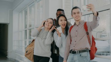 Grup dört çok etnik gruptan oluşan öğrenci üniversite koridorda duran smartphone makinesinde selfie alarak. Telefon ve arkadaşları olumlu poz hipster adam