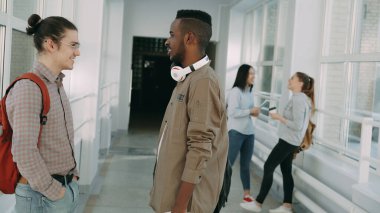 Beyaz ve Afro-Amerikan erkek öğrencilerin üniversite salonunda kapalı, iki kız yakınındaki sohbet durmuş ise konuşuyorum