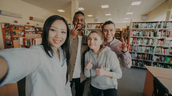 留学生グループの視点が楽しい笑顔と大学図書館室内でスマート フォンのカメラで Selfie 写真を撮って — ストック写真