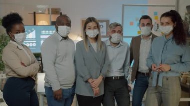 Kovid-19 salgını sırasında gece ofiste duran tıbbi maske takan iş adamlarının yavaş çekimde portresi. Çalışma ve sağlık konsepti.