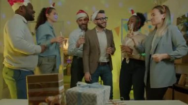 Çok ırklı iş adamları kadeh tokuşturup geceleri ofiste şampanya içiyorlar. Mutlu çalışanlar işyerinde yeni yılı kutluyor.