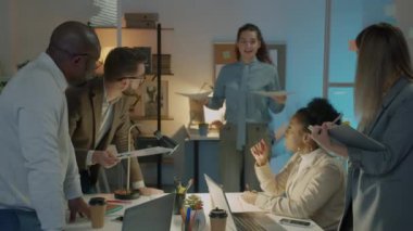 Bir grup ofis çalışanı belgelere bakıp geceleri karanlık işyerlerinde fikirlerini paylaşıyorlar. Çalışanlar iş birliğine odaklandı.