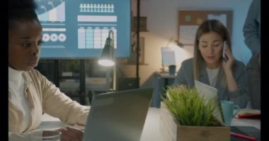 Hippi erkek öğrenci Üniversite Kütüphanesi sınavlarda için kapalı kitap okuyan sınıf arkadaşları ile hazırlarken dizüstü bilgisayar kullanan bardaklarda odaklanmak