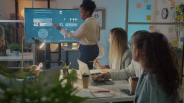 Ofis çalışanı dijital ekranı işaret ediyor ve geceleri toplantı odasında pazarlama fikirlerini tartışıyor. Yaratıcı ekip için sunum yapan genç bayan..